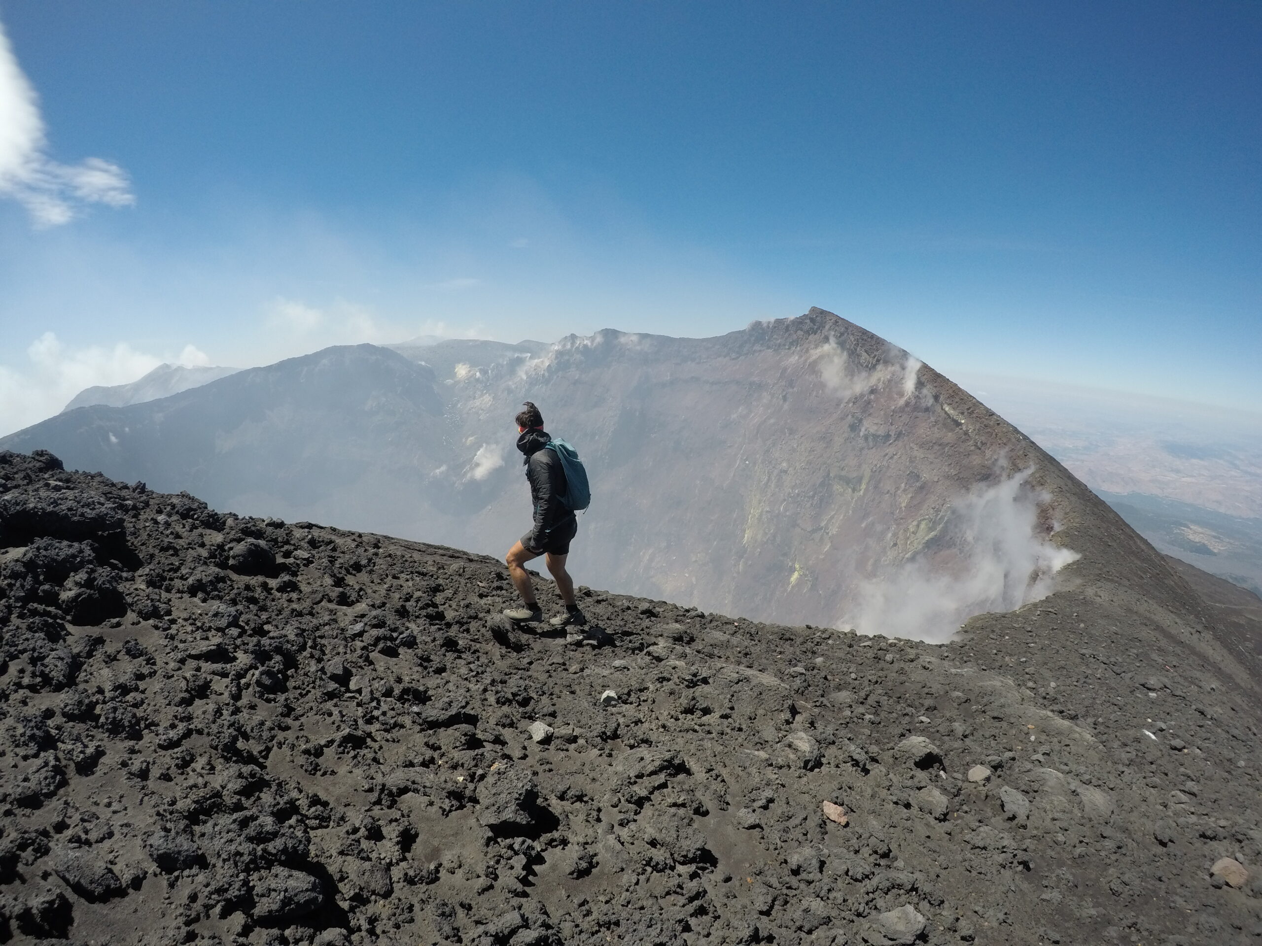 Rick Stack walking on the edge of Mount Etna's northern crater with smoke emerging in the background.