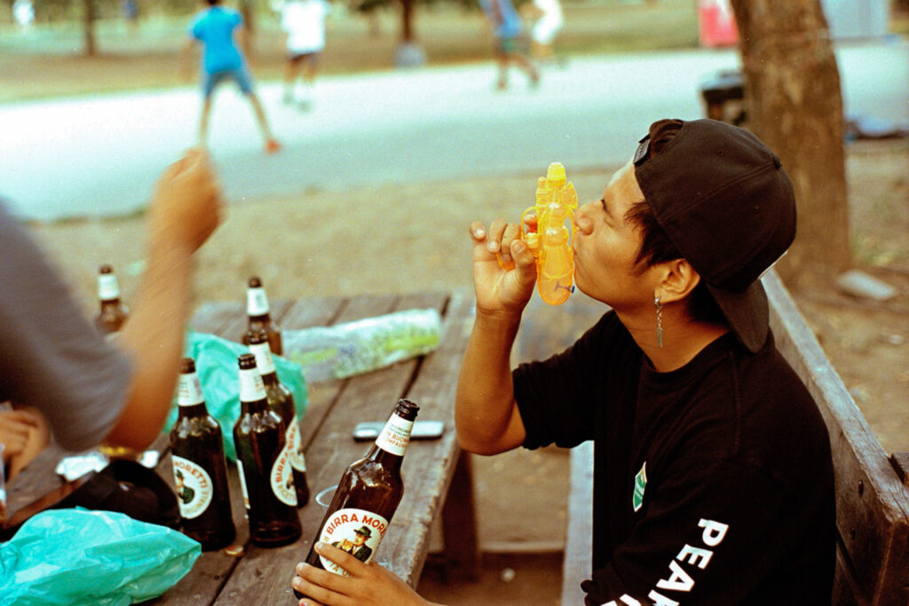 Young man kissing his light green water gun while holding a 66cl bottle of Moretti in Parco Martiri della Libertà Iracheni vittime del terrorismo, Milan, Italy